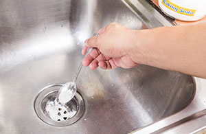 Hand pouring spoonful of baking soda down drain