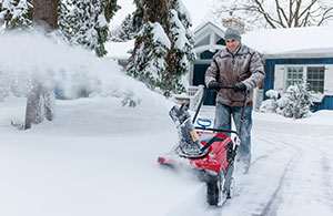 snow covered yard with a man using a snow blower to clean a path